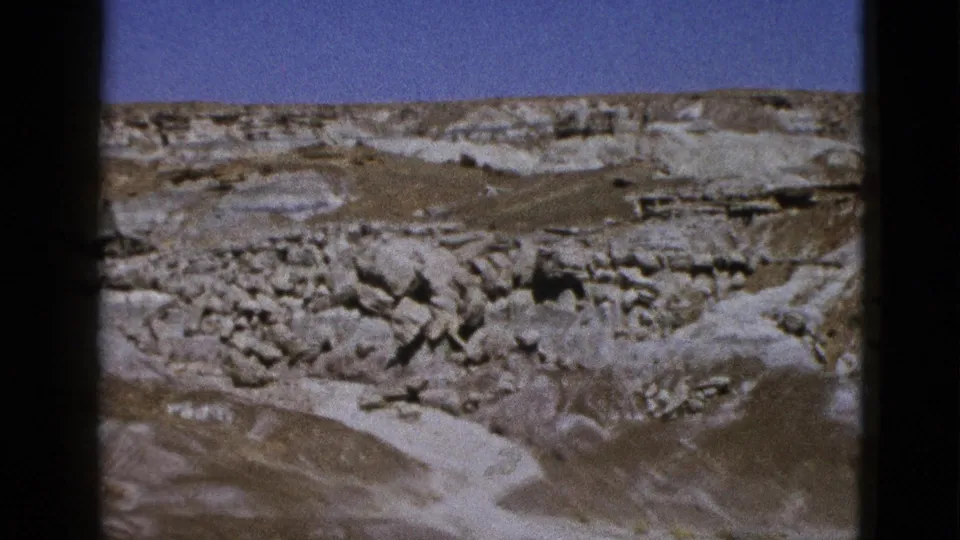 1953 California 8mm frame of an arid canyon landscape with pale rock shelves, boulders, and clear sky.