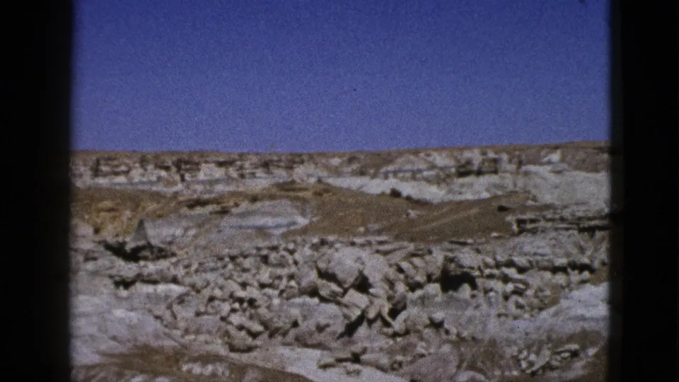 1953 California 8mm frame showing a dry canyon slope, pale rock formations, and a broad blue sky.