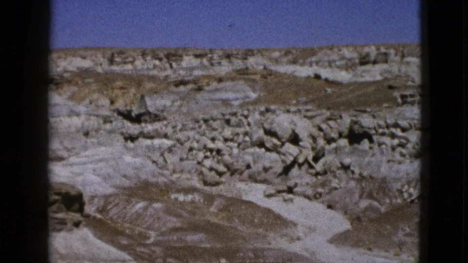 1953 California 8mm frame showing a pale canyon wash, rocky ledges, boulder clusters, and clear sky.