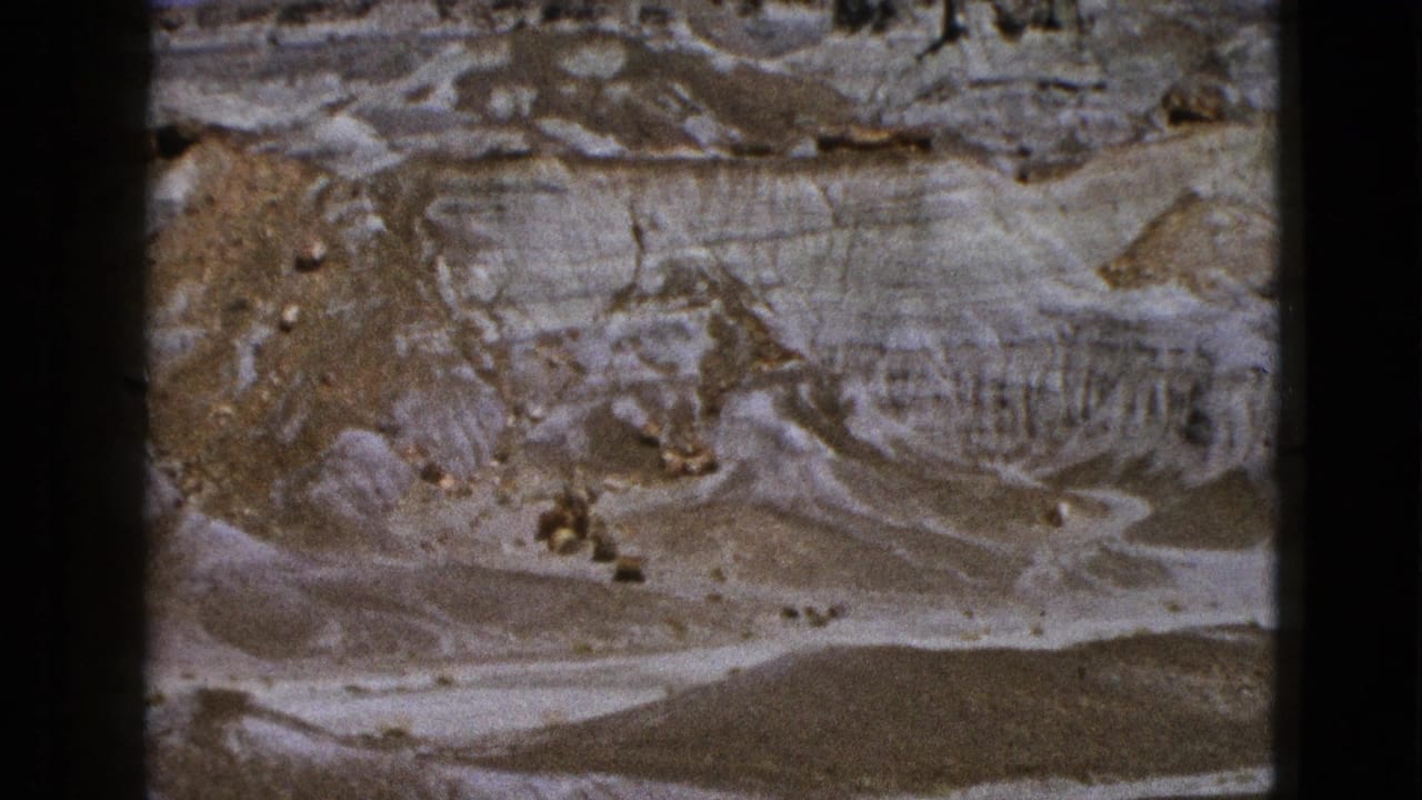 Aerial view of layered desert hills with pale gullies and darker rock ridges.