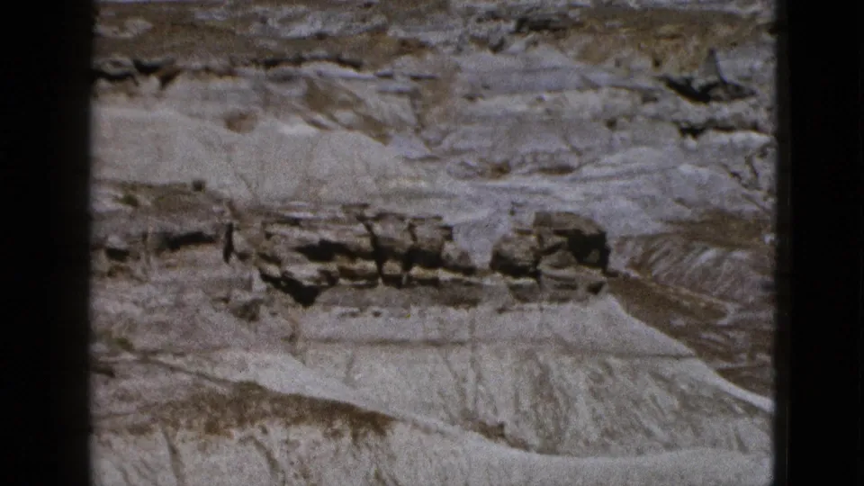 1953 Arizona aerial frame with a broad eroded bluff, pale sloping ground, dark horizontal strata, and arid terrain.