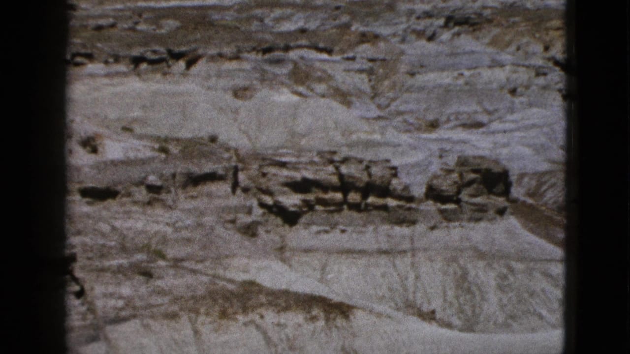 1953 Arizona 8mm frame showing pale eroded rock layers, darker outcrops, and visible black film-frame edges.