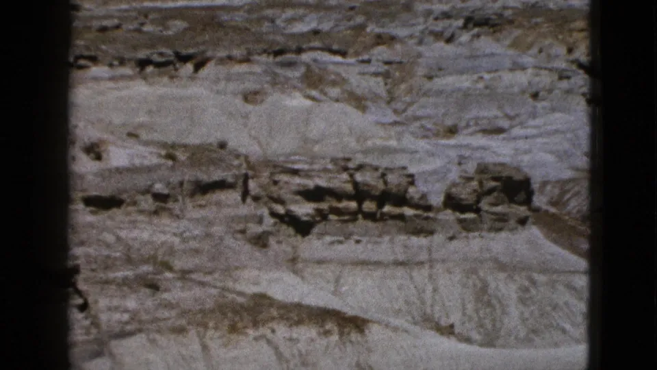 1953 Arizona 8mm frame showing pale eroded rock layers, darker outcrops, and visible black film-frame edges.