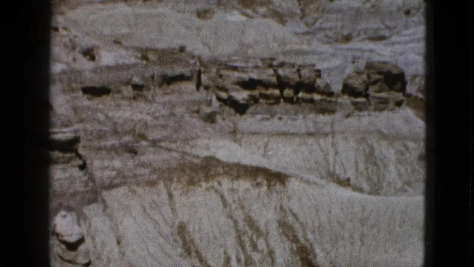 1953 Arizona 8mm frame with pale desert strata, rough ledges, and a narrow dark film border at the side.