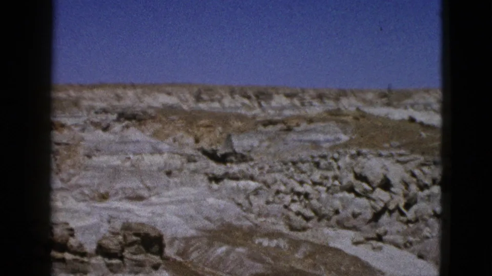 1953 Arizona 8mm frame looking across a rocky desert slope under deep blue sky and pale distant formations.