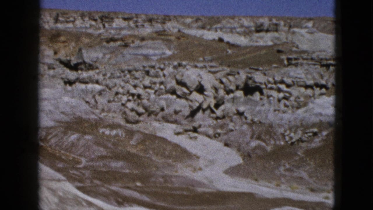 Layered desert rocks and dry wash-like terrain under clear sky.