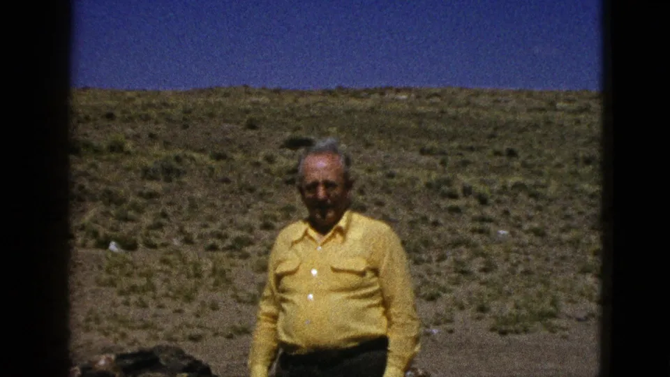 1953 Arizona home-movie frame of an adult man in a yellow shirt standing before scrub-covered desert hills.