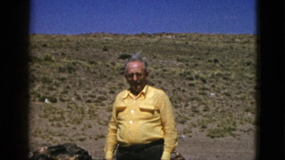 1953 Arizona home-movie frame showing an adult man in a yellow shirt centered against arid scrub and distant hills.