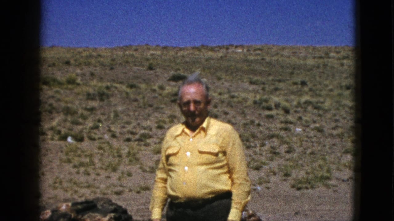 An older man in a yellow button-up shirt faces the camera in a sunny Arizona desert landscape, filmed on 8mm in 1953.