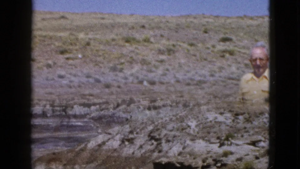 1953 Arizona home-movie frame showing part of the man at the right edge as the camera frames rocky desert terrain.