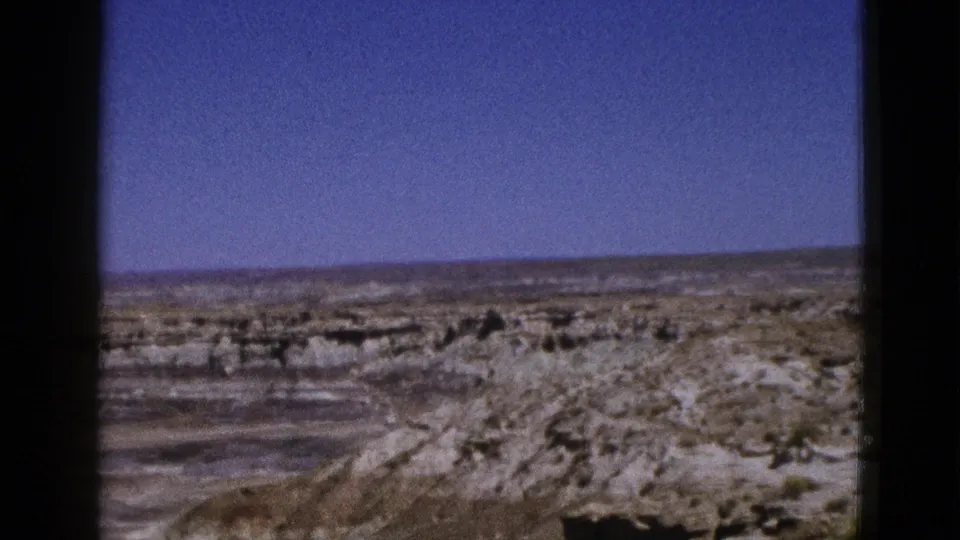 1953 Arizona home-movie frame showing a wide rocky desert panorama with scrubland and a clear blue sky.