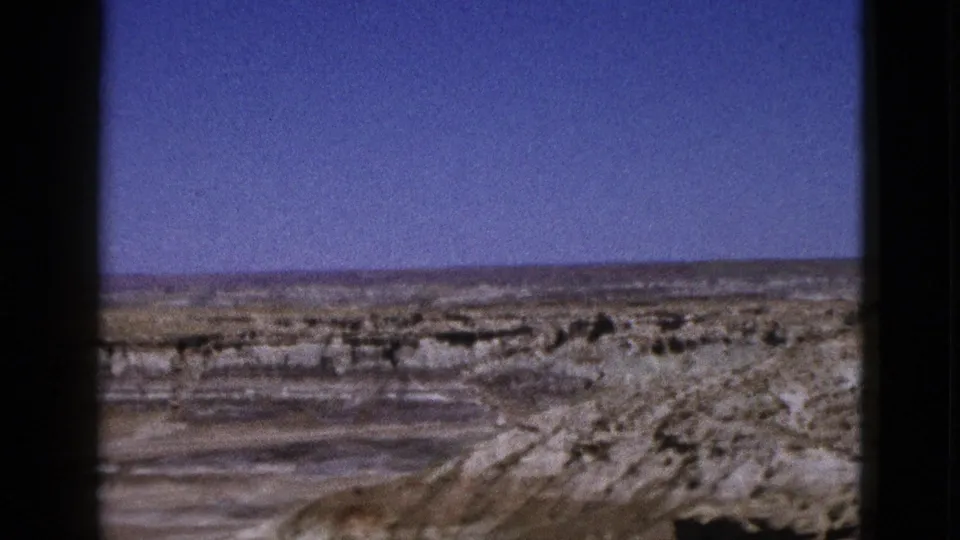 1953 Arizona 8mm view of dry flats and eroded pale rock formations framed by heavy black film edges.