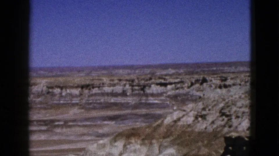 1953 Arizona home-movie frame showing a barren basin, low layered ridges, and open sky in a static wide view.