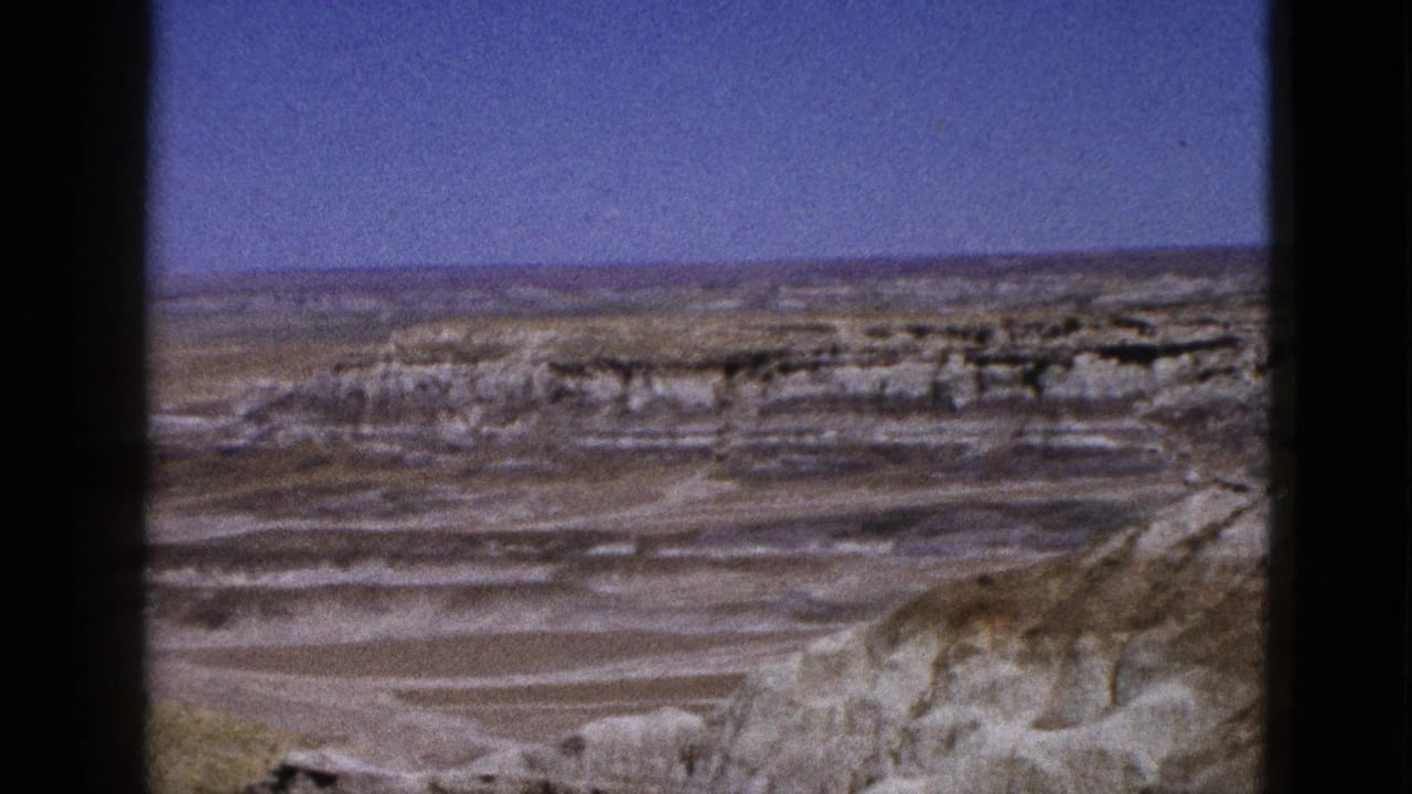 1953 Arizona 8mm frame showing a broad desert overlook with pale layered rock formations beneath a deep blue sky.