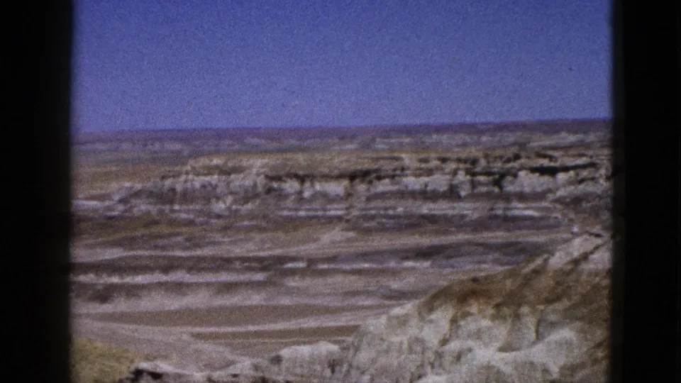 1953 Arizona 8mm frame showing a broad desert overlook with pale layered rock formations beneath a deep blue sky.