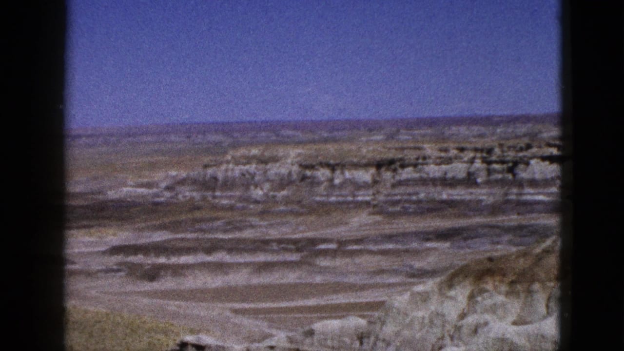 1953 Arizona home-movie frame with distant mesas, horizontal rock layers, and dry desert flats under clear sky.