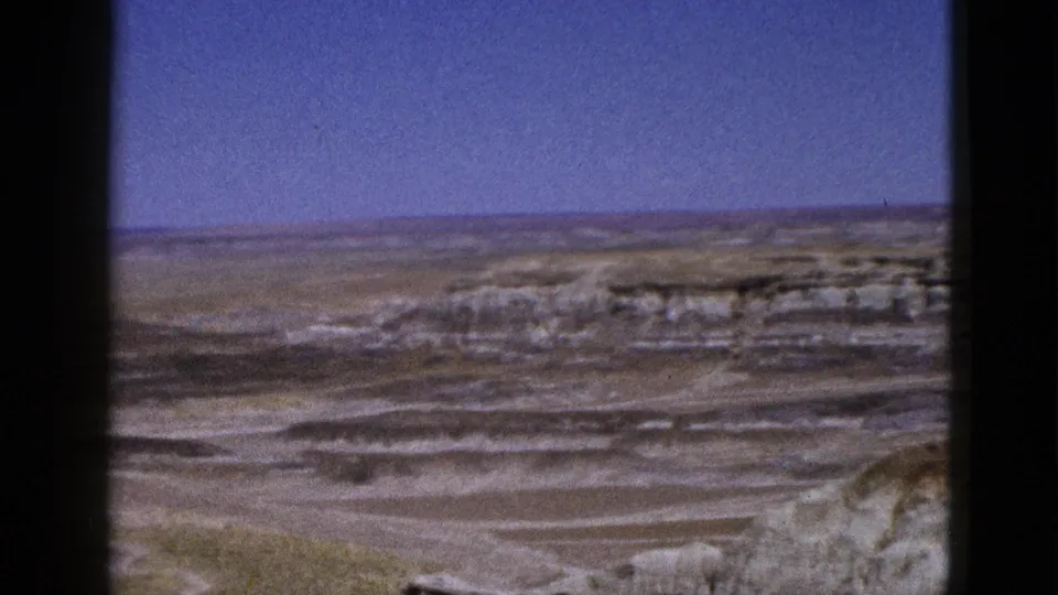 1953 Arizona 8mm frame showing a slightly shifted desert view with layered cliffs, scrub, and distant open land.
