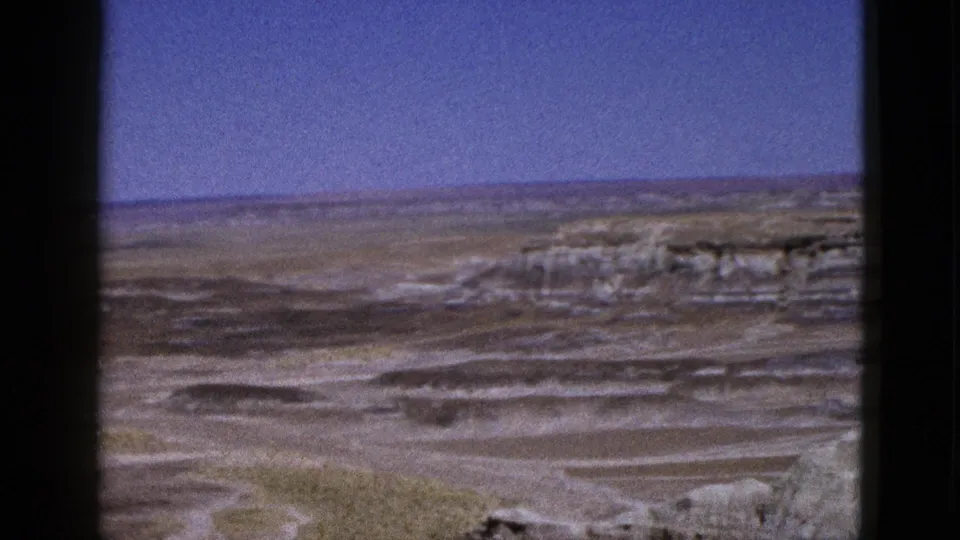 1953 Arizona home-movie frame holding on a broad arid vista with mesas, pale rock layers, and dry washes.