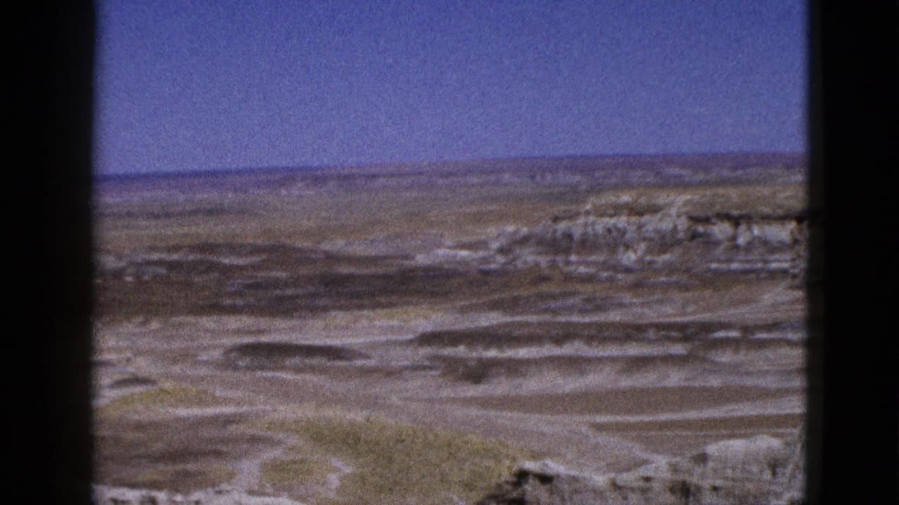 1953 Arizona 8mm frame showing a broad desert overlook with pale eroded ground, distant horizon, and dark contact-sheet borders.