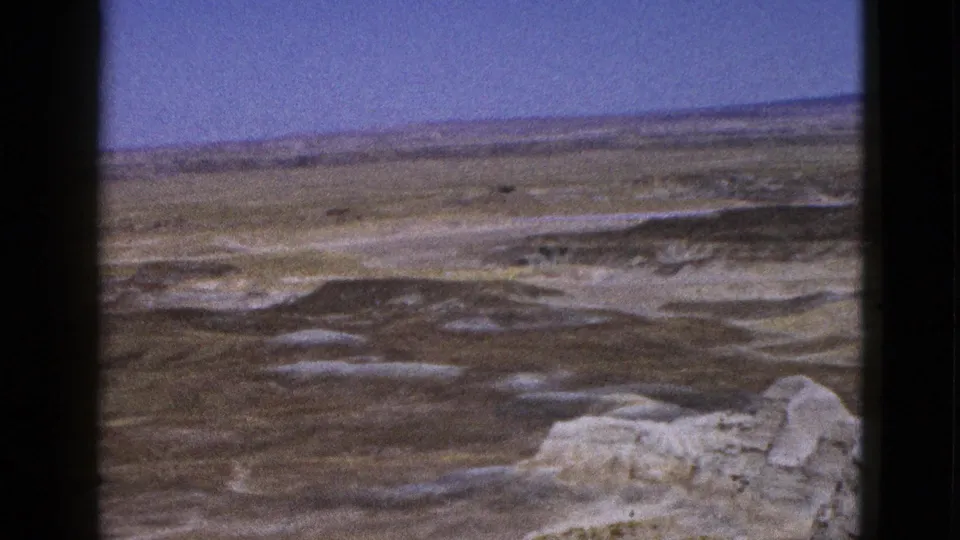 1953 Arizona 8mm frame showing pale foreground outcrops, layered desert terrain, and a low horizon in soft amateur-film focus.