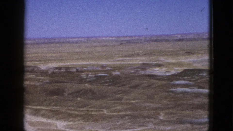 Final 1953 Arizona desert view showing broad dry terrain, faint washes, and a low horizon in grainy 8mm color.