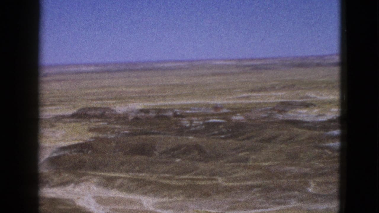 Wide desert landscape with scrubby ridges, pale sand channels, and clear sky.