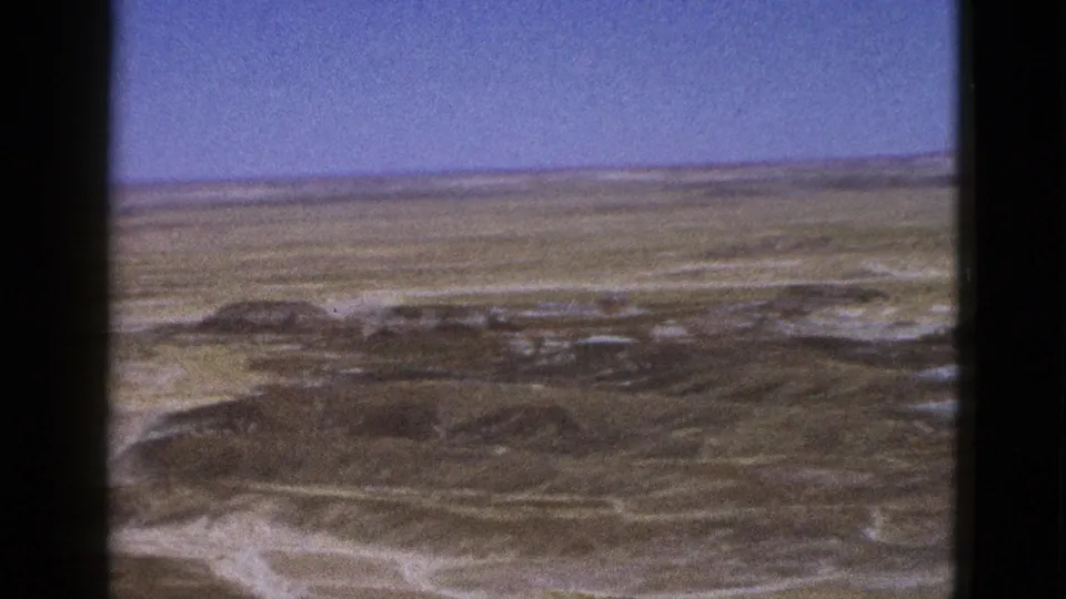 Wide 1953 Arizona desert view showing scrub-covered ridges, light sand channels, and a broad blue sky.