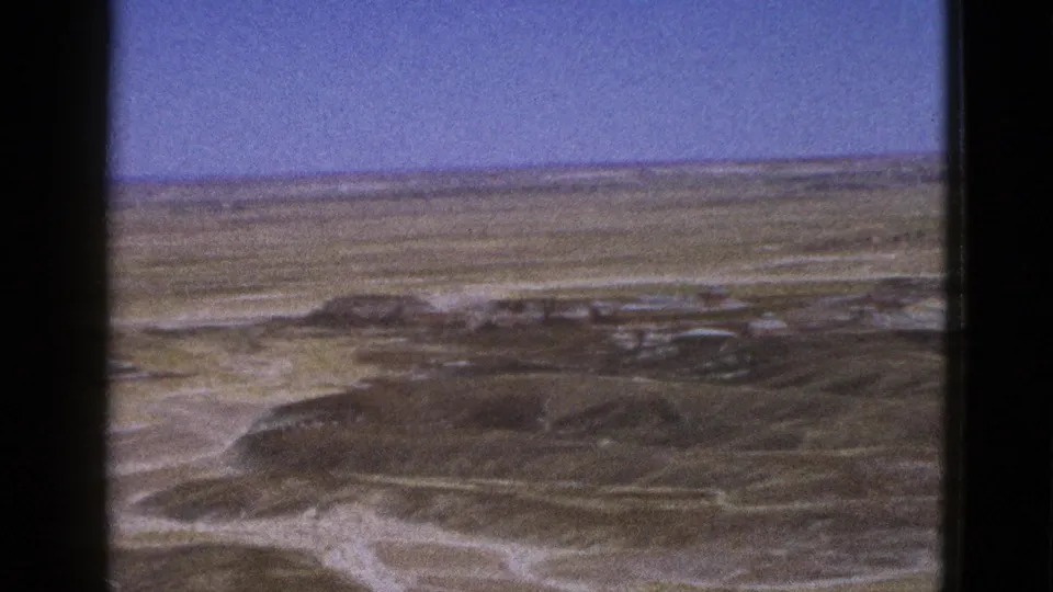 Soft 8mm frame of Arizona desert hills, pale foreground sand, and open blue sky from 1953 home-movie footage.