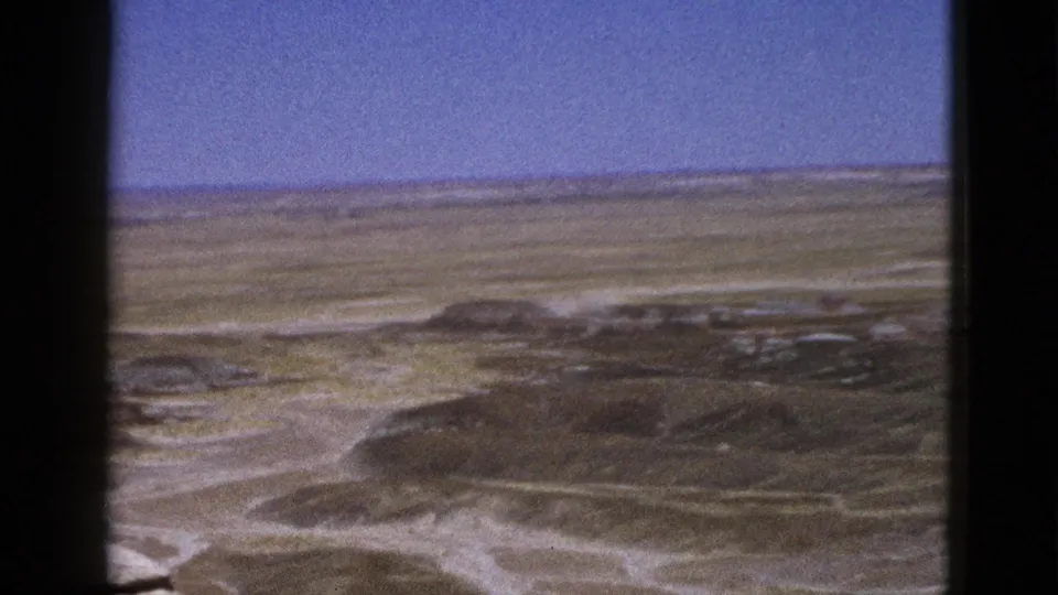 1953 Arizona desert frame with a low ridge, pale wash patterns, scrub texture, and black 8mm film borders.
