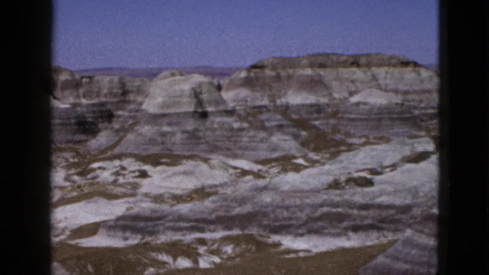 1953 Arizona home-movie still showing dry desert washes below layered mesas and pale eroded hills.