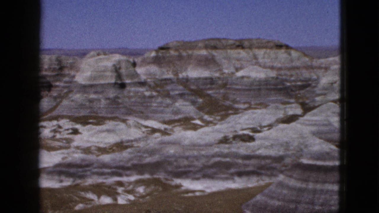 Layered pale canyon hills and rounded eroded formations beneath a blue sky.