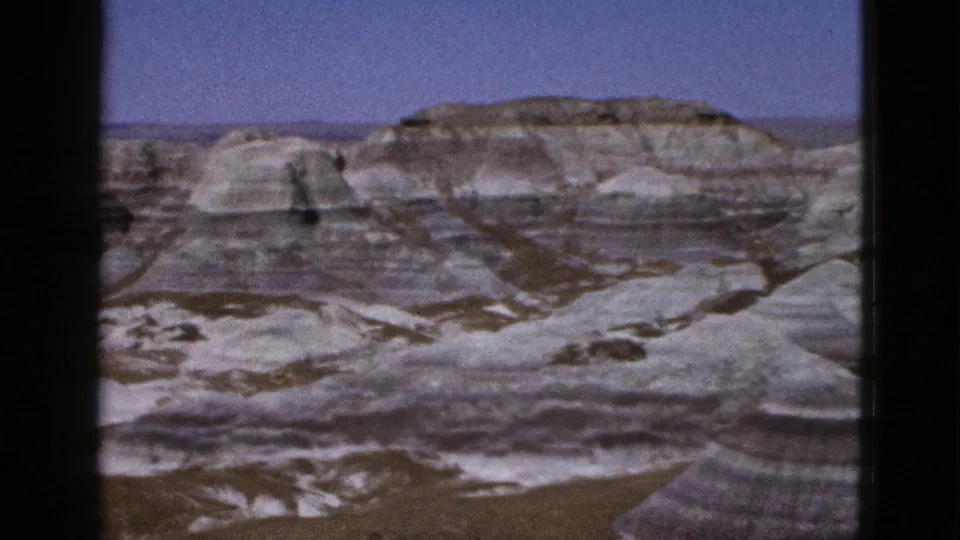 1953 8mm view of Arizona desert canyon terrain with pale layered hills, rounded formations, and a clear blue sky.