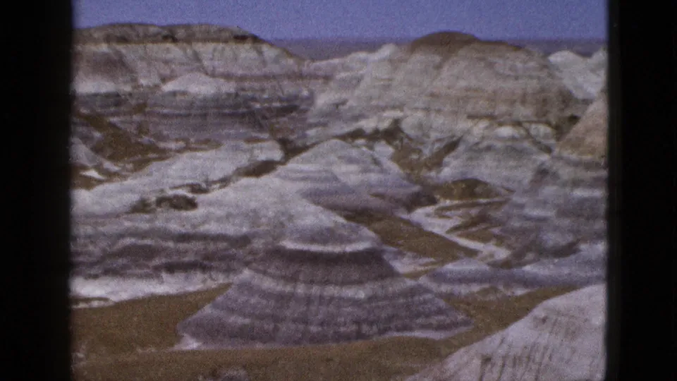 Wide 1953 8mm Arizona canyon view with banded eroded hills, dry gullies, pale rock, and visible film frame borders.