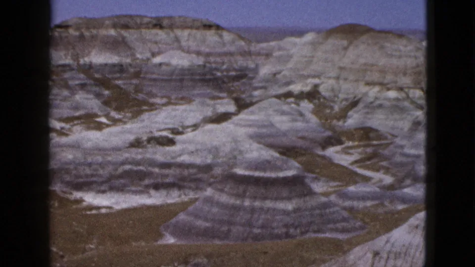 1953 Arizona 8mm frame showing pale layered badlands and rounded eroded rock forms under a clear blue sky.