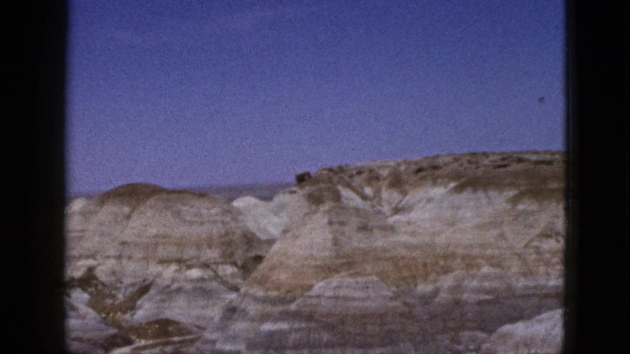 1953 Arizona home-movie frame with eroded desert hills, visible horizontal bands, and open sky.