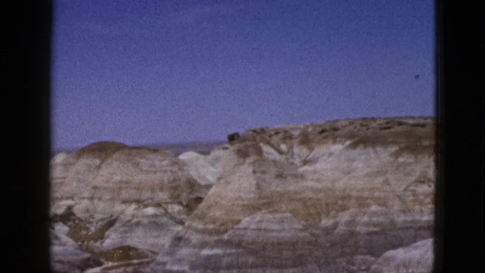 1953 Arizona home-movie frame with eroded desert hills, visible horizontal bands, and open sky.