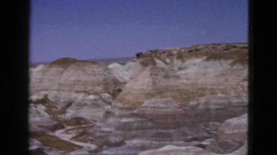 1953 Arizona 8mm frame showing a wide, soft-focused view of rounded desert ridges and layered rock surfaces.