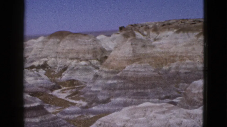1953 Arizona frame showing layered desert hills, dry gullies, and muted earth tones across a remote badlands view.