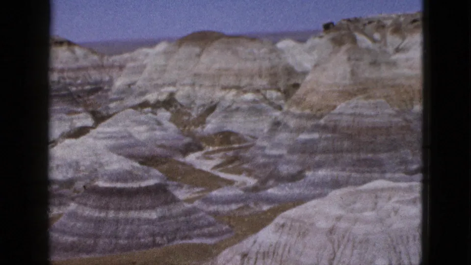 1953 Arizona 8mm still with soft grain over banded badlands, dry channels, and distant pale ridges.