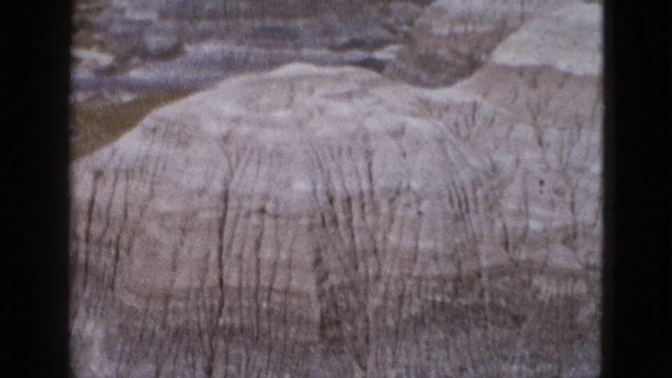 1953 Arizona footage showing a rounded pale rock formation with vertical erosion streaks and layered terrain behind it.