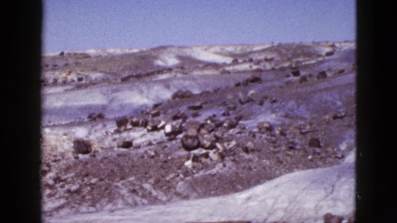 1953 Arizona 8mm frame showing a barren rocky hill with patches of snow beneath a clear blue sky.
