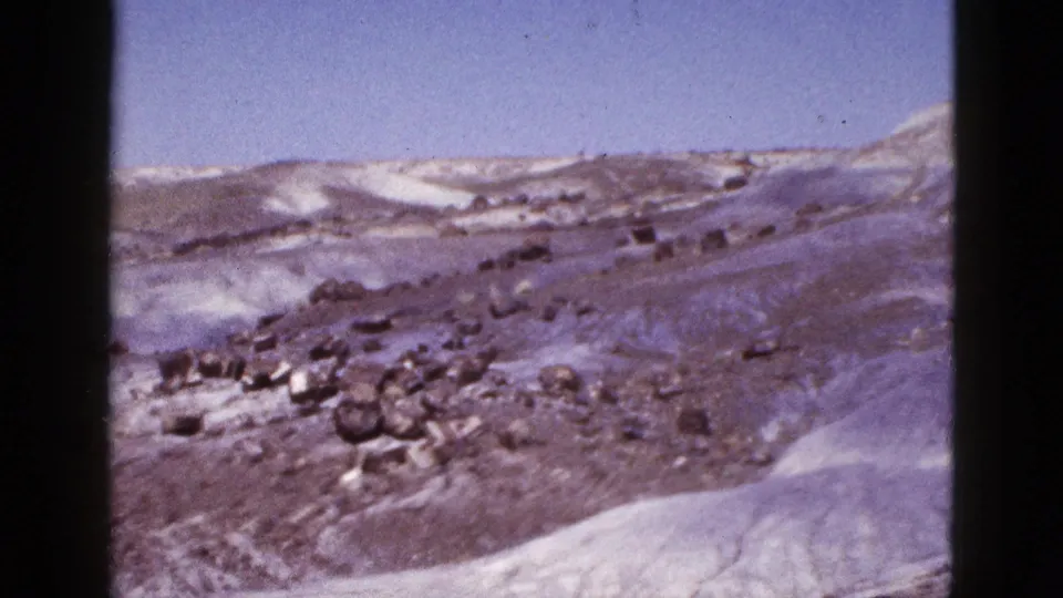 Arizona home-movie frame from 1953 showing a snow-patched rocky slope and pale ridge beneath blue sky.