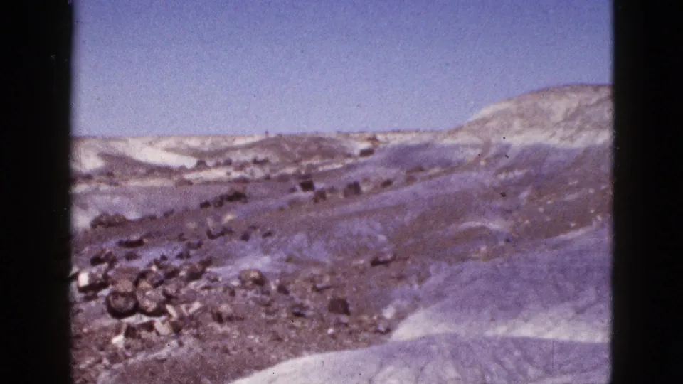 1953 Arizona 8mm still with dark rocks in the foreground and snow-streaked rolling hills beyond.