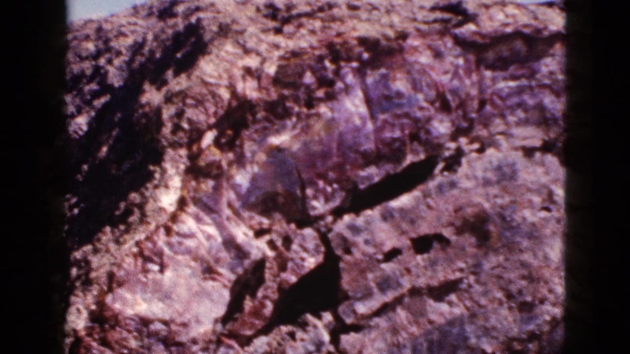 1953 Arizona 8mm frame showing a close, soft-focus view of layered desert rock with dark fissures and faded color.