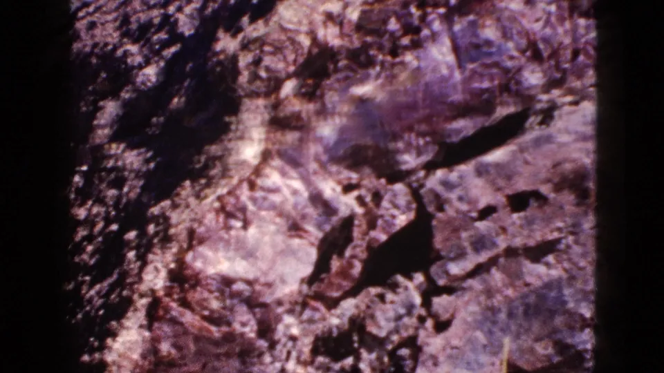 1953 Arizona 8mm still showing rough layered stone, dark crevices, and visible frame edge from a close handheld view.