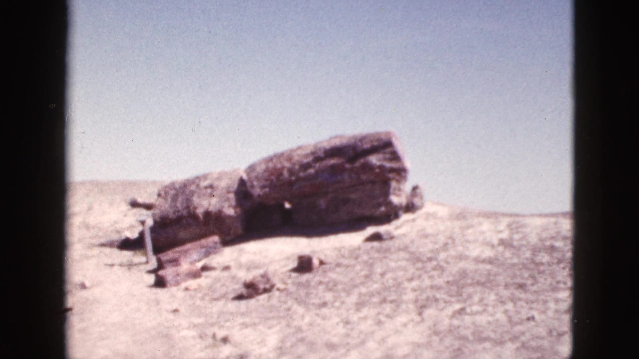 1953 Arizona 8mm frame showing a large weathered stone formation on a sunlit dry hillside with scattered rocks and sparse scrub.