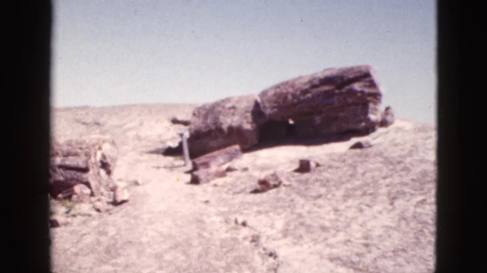 1953 Arizona home-movie frame showing the camera closer to the weathered stone formation on a dry hillside with small rocks and faint scrub visible.