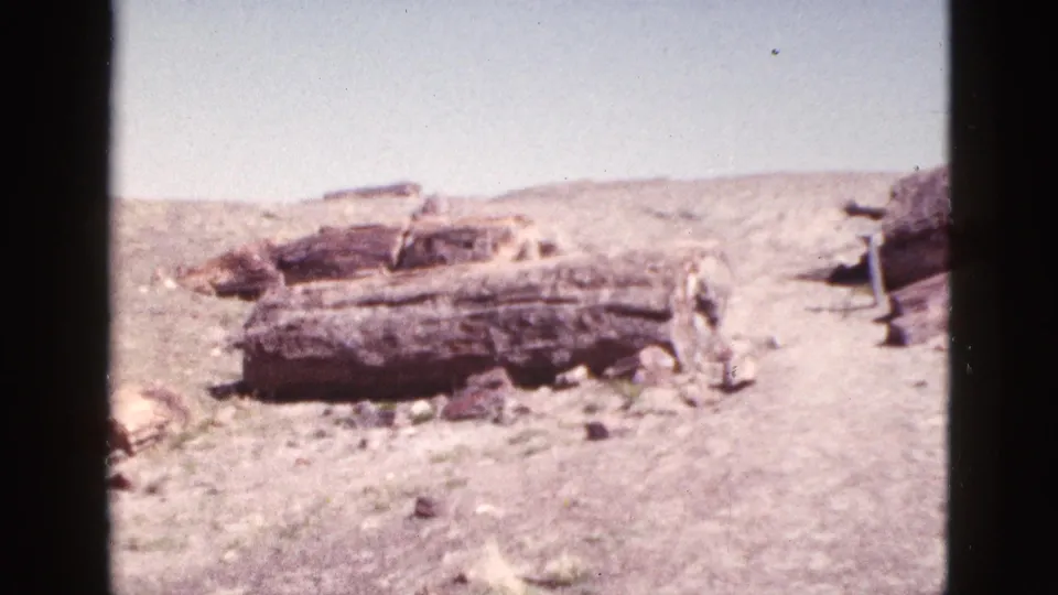 1953 Arizona 8mm frame showing multiple weathered stone sections on an arid hillside, with open sky and sparse desert vegetation in the background.