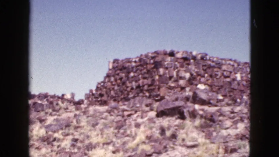 1953 Arizona 8mm frame showing a weathered stone ruin on a dry, rocky hill with sparse grass and open sky.