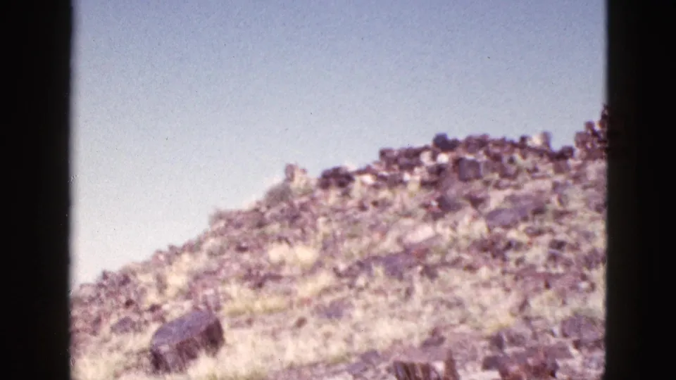 1953 Arizona home-movie frame of a dry rocky hill with remnants of stonework along the skyline.